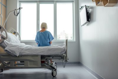 Back of senior lady sitting on hospital bed